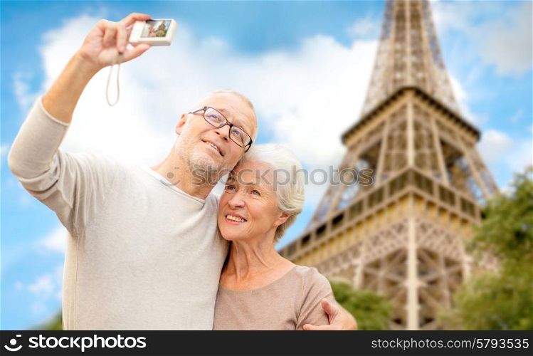 age, tourism, travel, technology and people concept - senior couple with camera taking selfie on street over eiffel tower background