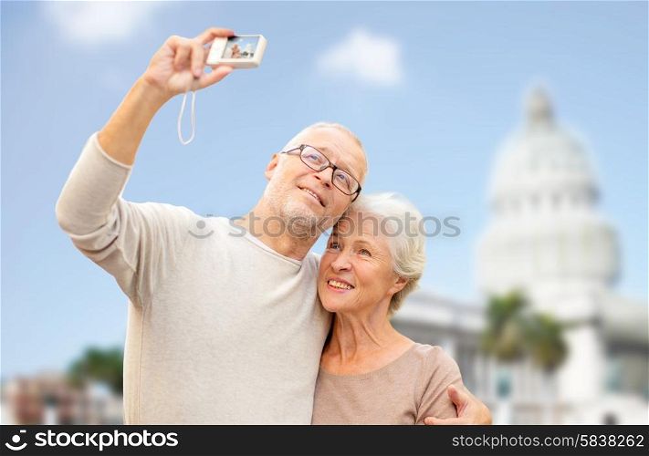 age, tourism, travel, technology and people concept - senior couple with camera taking selfie on street over washington white house background