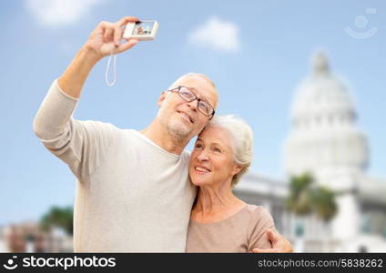 age, tourism, travel, technology and people concept - senior couple with camera taking selfie on street over washington white house background