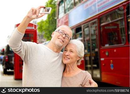 age, tourism, travel, technology and people concept - senior couple with camera taking selfie over london city street background