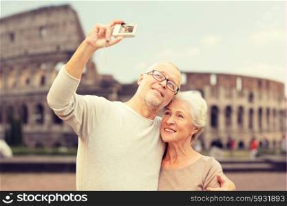 age, tourism, travel, technology and people concept - senior couple with camera taking selfie on street over coliseum background
