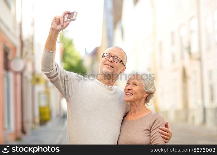 age, tourism, travel, technology and people concept - senior couple with camera taking selfie on street