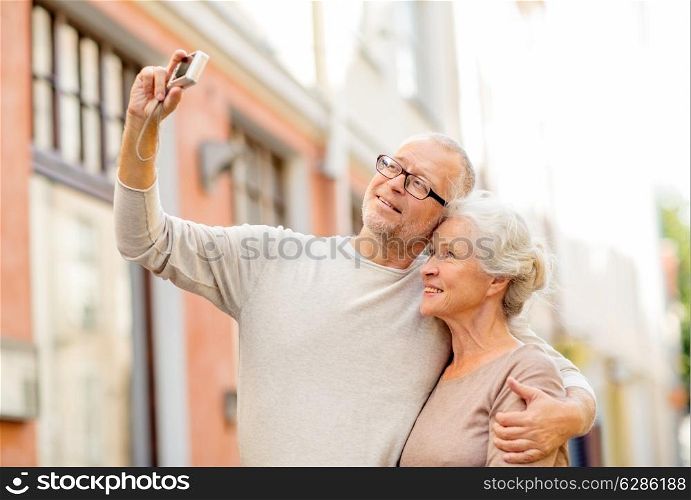 age, tourism, travel, technology and people concept - senior couple with camera taking selfie on street