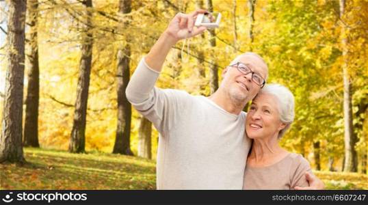age, tourism, travel, technology and people concept - senior couple with camera taking selfie on street. senior couple taking selfie in autumn park