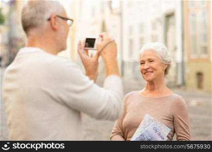 age, tourism, travel, technology and people concept - senior couple with map and camera photographing on street