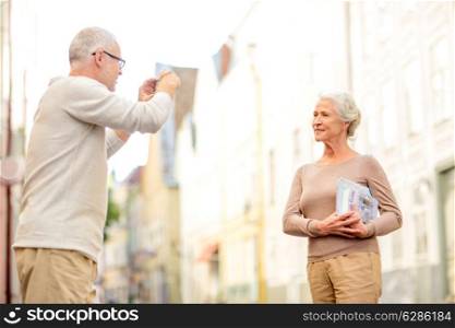 age, tourism, travel, technology and people concept - senior couple with map and camera photographing on street