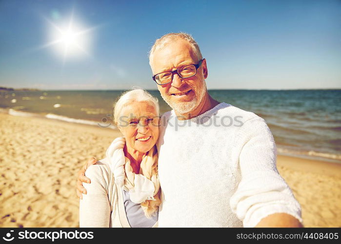 age, travel, tourism, technology and people concept - happy senior couple taking picture with smartphone selfie stick on summer beach