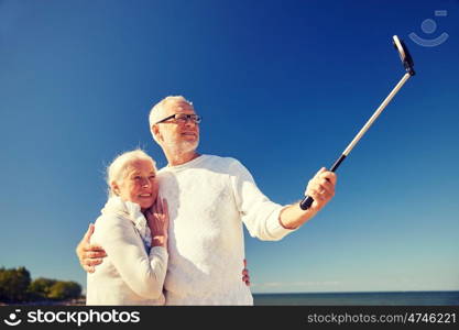 age, travel, tourism, technology and people concept - happy senior couple with smartphone on selfie stick taking picture on summer beach