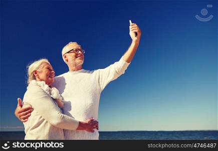 age, travel, tourism, technology and people concept - happy senior couple with smartphone taking selfie on summer beach