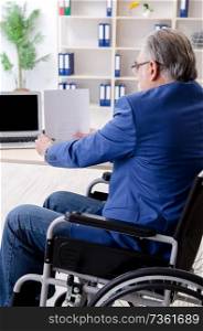 Aged employee in wheelchair working in the office 