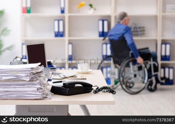 Aged employee in wheelchair working in the office 