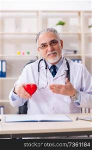 Aged male doctor cardiologist with heart model 