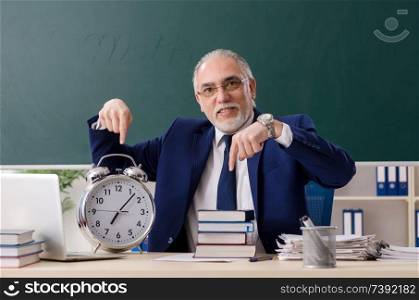 Aged male teacher in front of chalkboard 