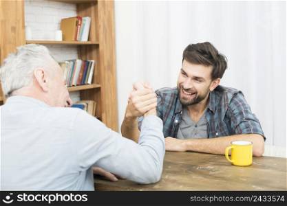 aged man young happy guy with hands clasped arm wrestling challenge table room