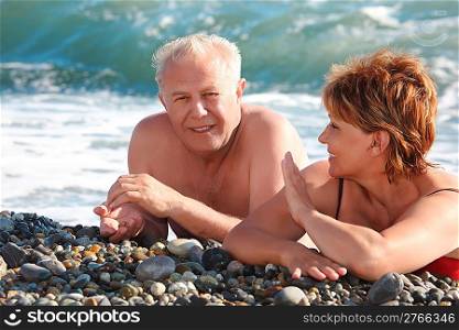 aged pair lie on pebble beach
