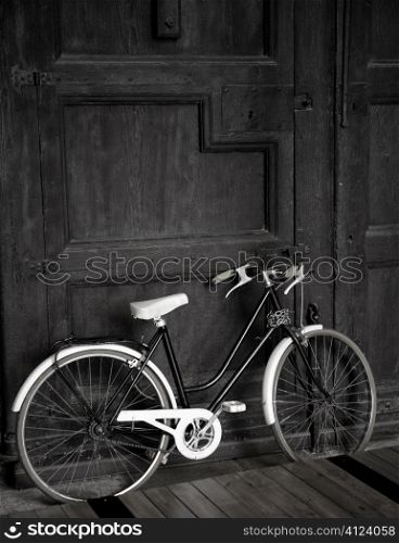 Aged vintage black bicycle, big wooden door, black and white