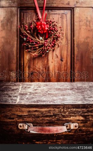 Aged vintage wooden suitcase at rustic background with Christmas wreath. Holiday Concepts Travel .