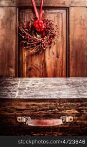 Aged vintage wooden suitcase at rustic background with Christmas wreath. Holiday Concepts Travel .