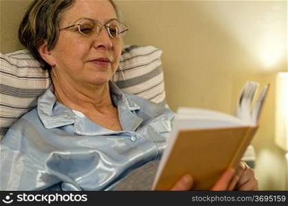 Aged woman reading book in bed in residential home