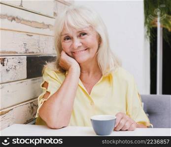 aged woman sitting kitchen with cup smiling