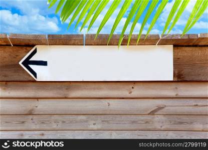 aged wood arrow direction sign on summer blue sky and palm tree leave