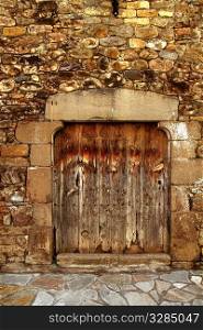 Aged wood door in medieval masonry Pyrenees house facade