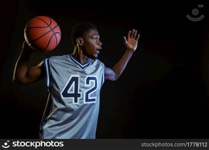 Aggressive basketball player poses with ball in studio, black background. Professional male baller in sportswear playing sport game, tall sportsman. Aggressive basketball player poses with ball