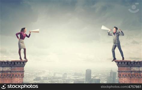 Aggressive communication. Young businessman and businesswoman on building top screaming on each other in paper trumpets