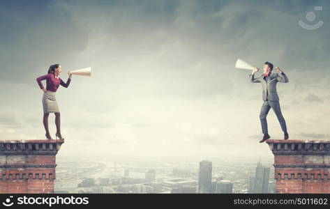 Aggressive communication. Young businessman and businesswoman on building top screaming on each other in paper trumpets