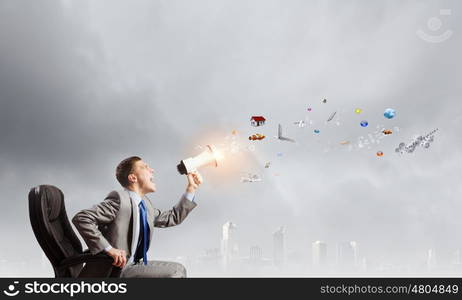 Aggressive management. Young angry businessman sitting on chair and screaming in megaphone