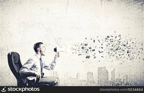 Aggressive management. Young angry businessman sitting on chair and screaming in megaphone