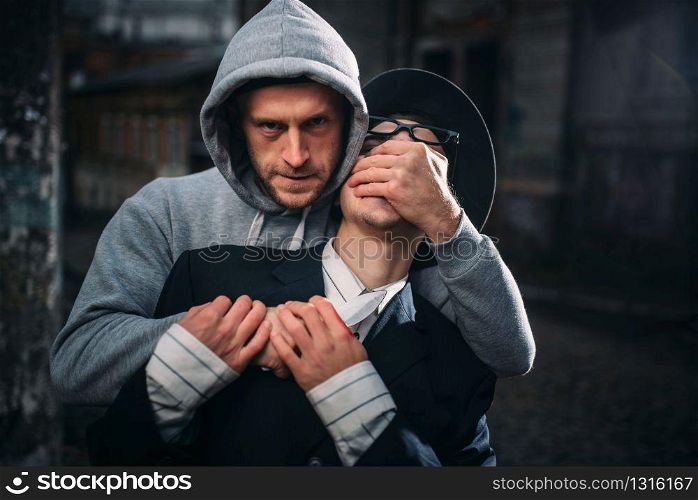 Aggressive thief with knife attack his victim on the night street. Gangster commits a robbery attack on a man. Crime concept. Thief with knife attack his victim on night street