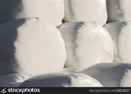 Agricultural background from many straw packages. Cereal bale of hay wrapped in plastic white foil.. Bale of hay wrapped in plastic foil