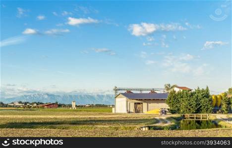 Agricultural landscape with river,mountains and farm with tractor and silos. And solar panels on the roof