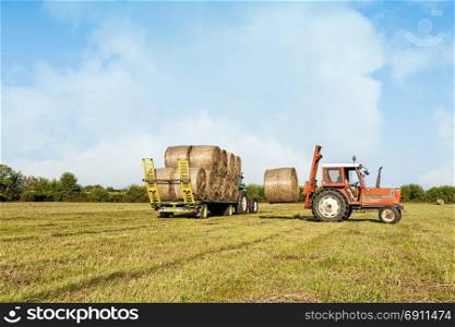 Agricultural scene. Tractor collecting hay bales in field and loading on farm wagon.