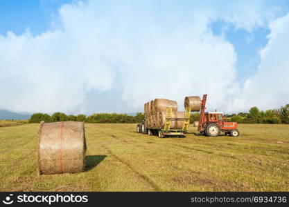 Agricultural scene. Tractor collecting hay bales in field and loading on farm wagon.