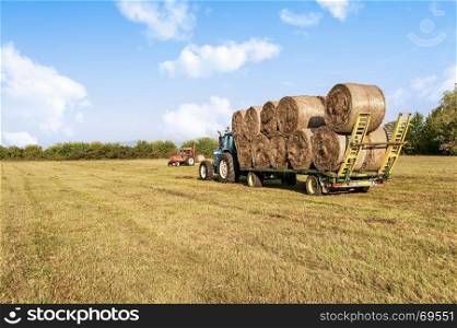 Agricultural scene. Tractor collecting hay bales in field and loading on farm wagon.
