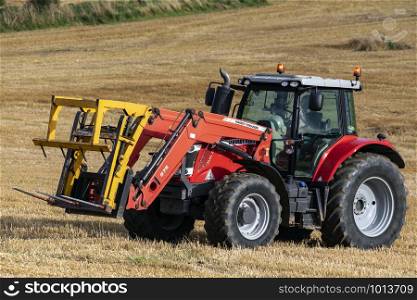 Agriculture - a tractor collecting bales of hay following the harvesting of a field of wheat on farmland in North Yorkshire in the United Kingdom.