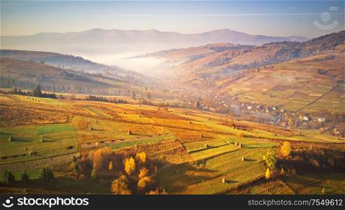 Agriculture fields on the hills. Panorama of beautiful autumn mountains. Misty rural scene in the morning. Sunrise over mountain foggy valley. Carpathians, Ukraine