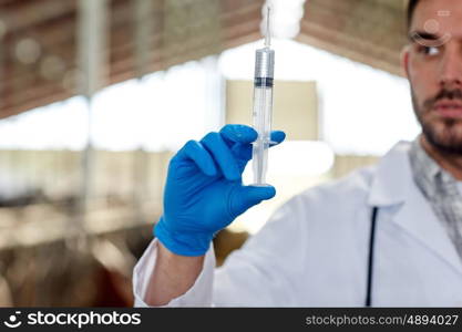 agriculture industry, farming, medicine, animal vaccination and people concept - close up of veterinarian or doctor hand with vaccine in syringe at cowshed on dairy farm