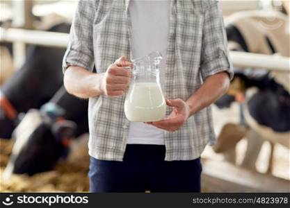 agriculture industry, farming, people and animal husbandry concept - close up of young man or farmer with cows milk in jug at cowshed on dairy farm
