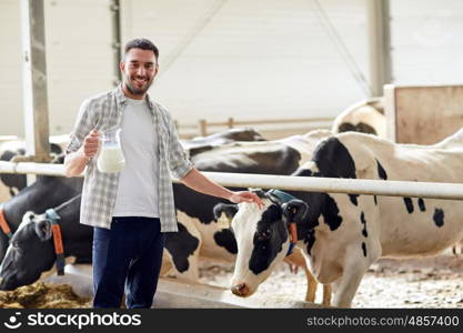 agriculture industry, farming, people and animal husbandry concept - happy smiling young man or farmer with cows milk in jug at cowshed on dairy farm