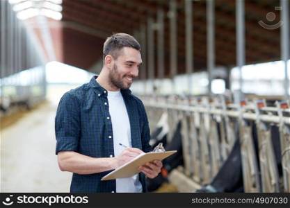agriculture industry, farming, people and animal husbandry concept - happy smiling young man or farmer with clipboard and cows in cowshed on dairy farm. farmer with clipboard and cows in cowshed on farm