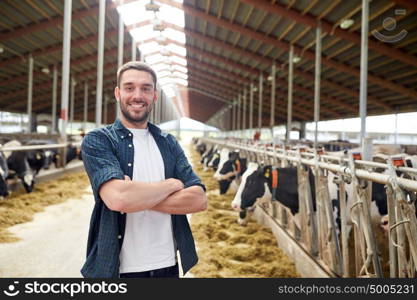 agriculture industry, farming, people and animal husbandry concept - happy smiling young man or farmer with herd of cows in cowshed on dairy farm. man or farmer with cows in cowshed on dairy farm