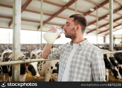 agriculture industry, farming, people and animal husbandry concept - happy young man or farmer drinking cows milk from jug in cowshed on dairy farm