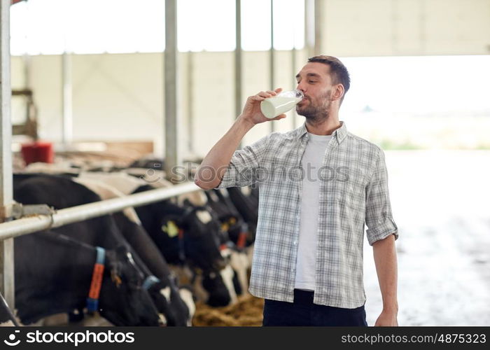 agriculture industry, farming, people and animal husbandry concept - happy young man or farmer drinking cows milk from bottle in cowshed on dairy farm