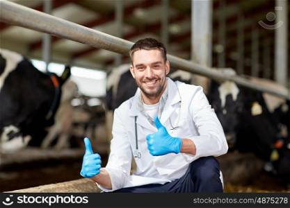 agriculture industry, farming, people and animal husbandry concept - veterinarian or doctor and cows in cowshed on dairy farm showing thumbs up hand sign