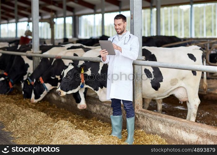 agriculture industry, farming, people and animal husbandry concept - veterinarian or doctor with tablet pc computer and herd of cows in cowshed on dairy farm