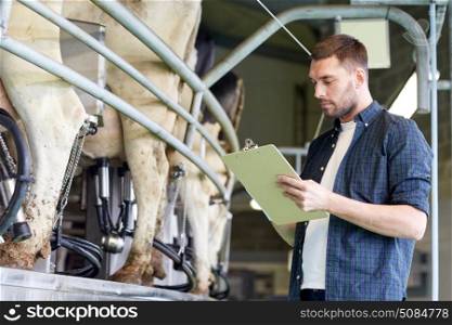 agriculture industry, farming, people, milking and animal husbandry concept - young man or farmer with clipboard and cows at rotary parlour system on dairy farm. man with clipboard and milking cows on dairy farm. man with clipboard and milking cows on dairy farm