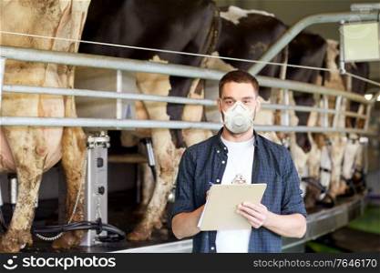 agriculture industry, farming, people, milking and animal husbandry concept - young man or farmer with clipboard and cows at rotary parlour system on dairy farm wearing mask for protection from virus. man in mask with clipboard and cows on dairy farm